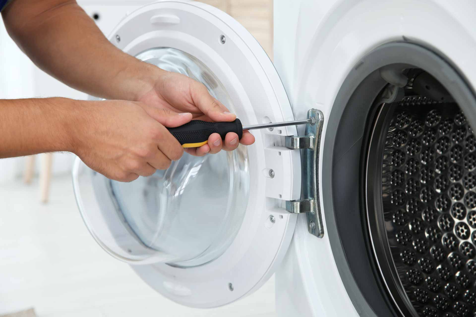 a man is using a screwdriver to fix a washing machine.