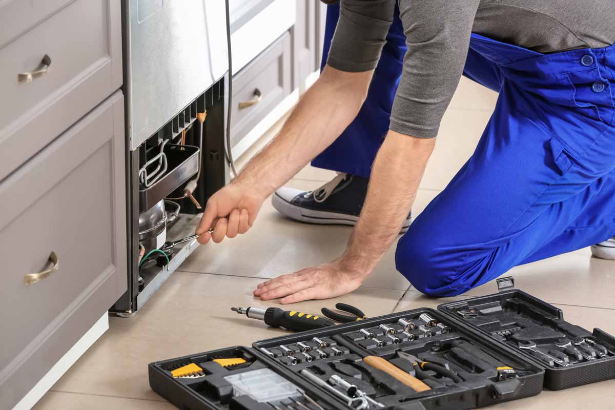 a man fixing a refrigerator in a kitchen