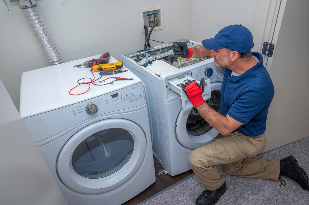 a man fixing a washing machine in a room.