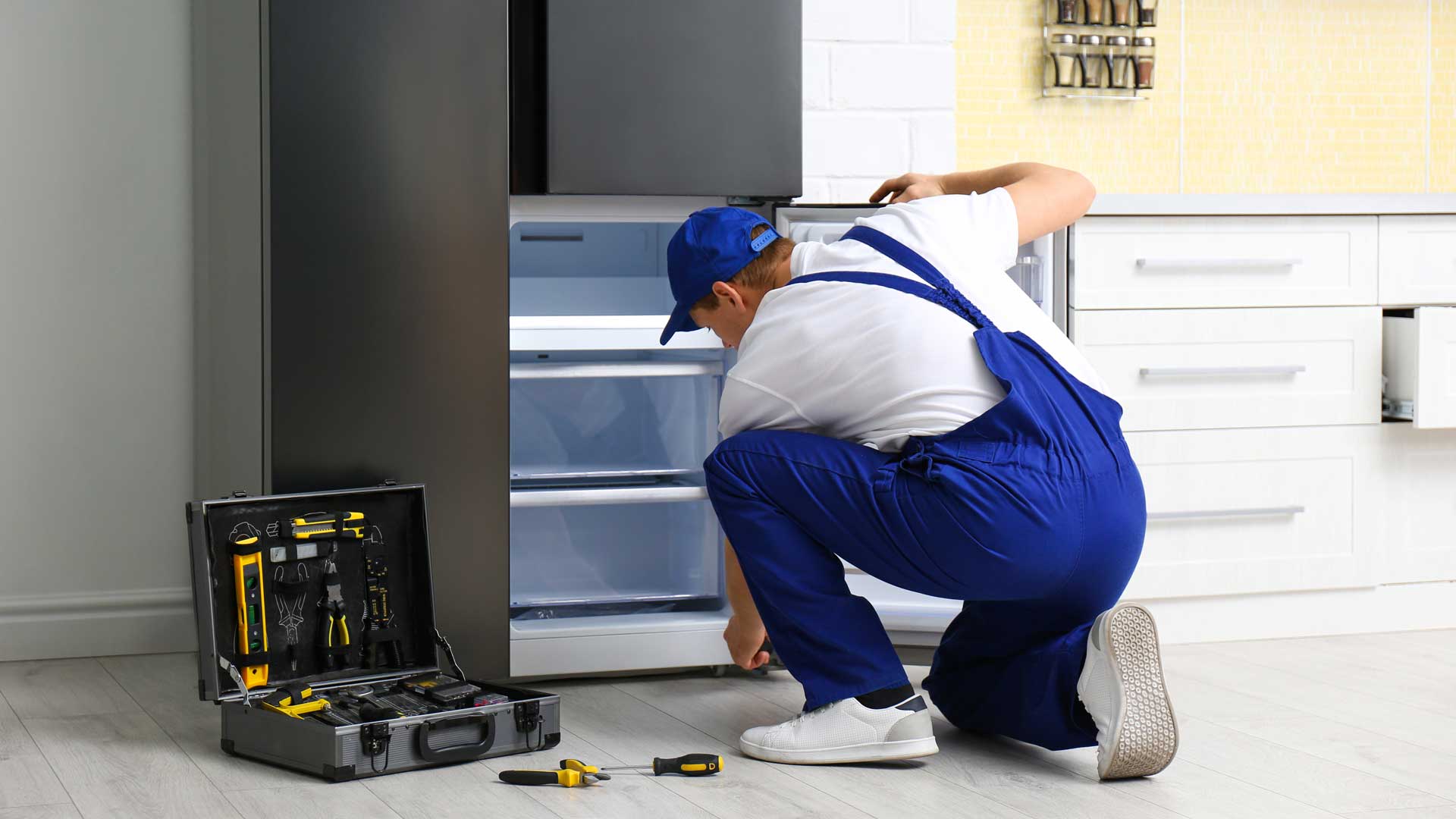 a man fixing a refrigerator in a kitchen