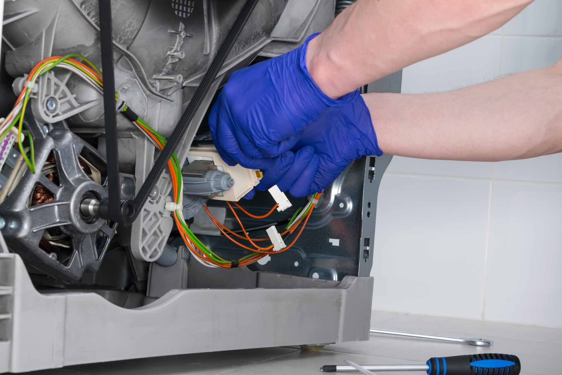 Appliance repair technician wearing blue gloves works on a washer/dryer